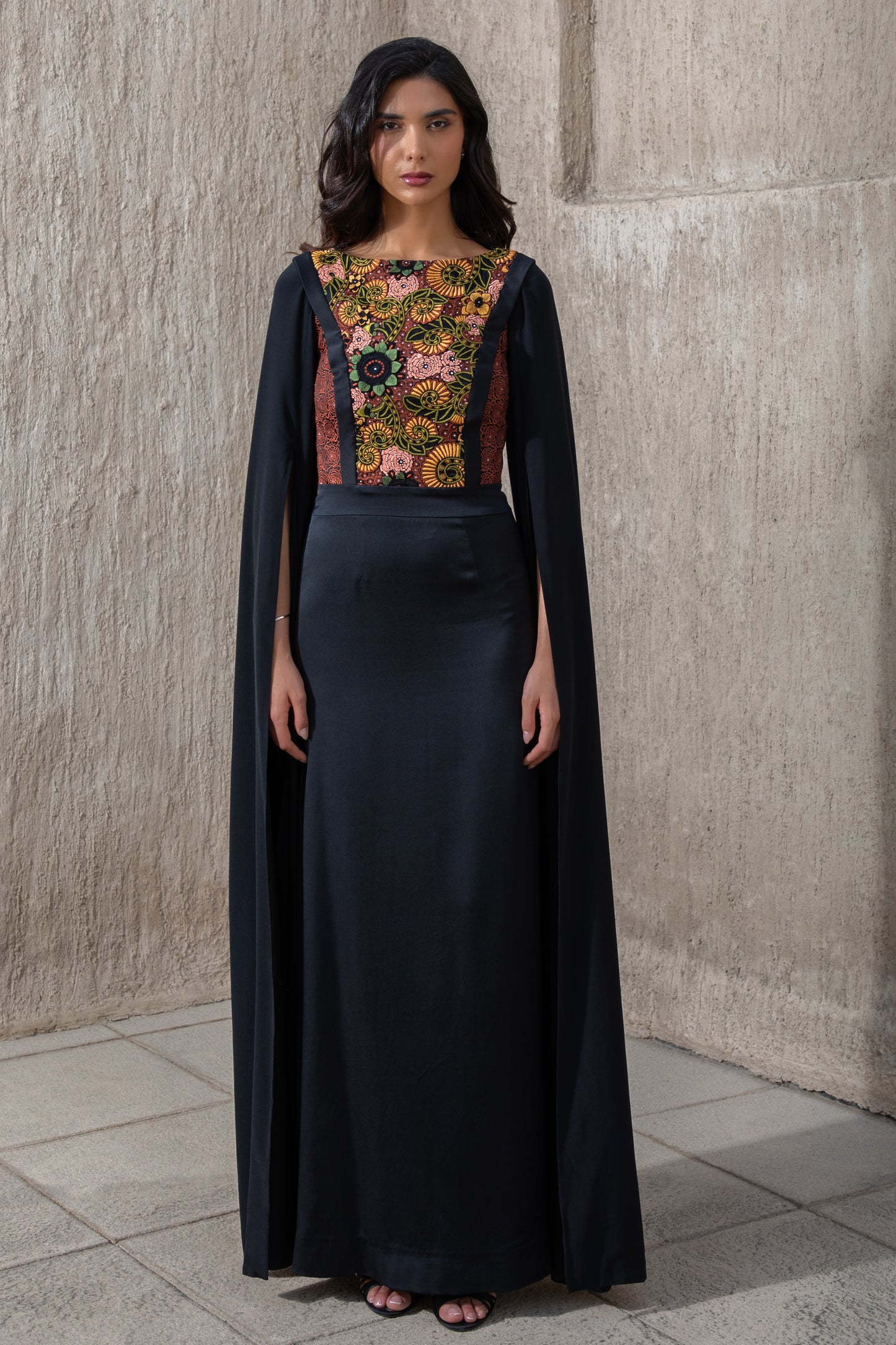 Model in black evening gown with floral embroidery and cape sleeves