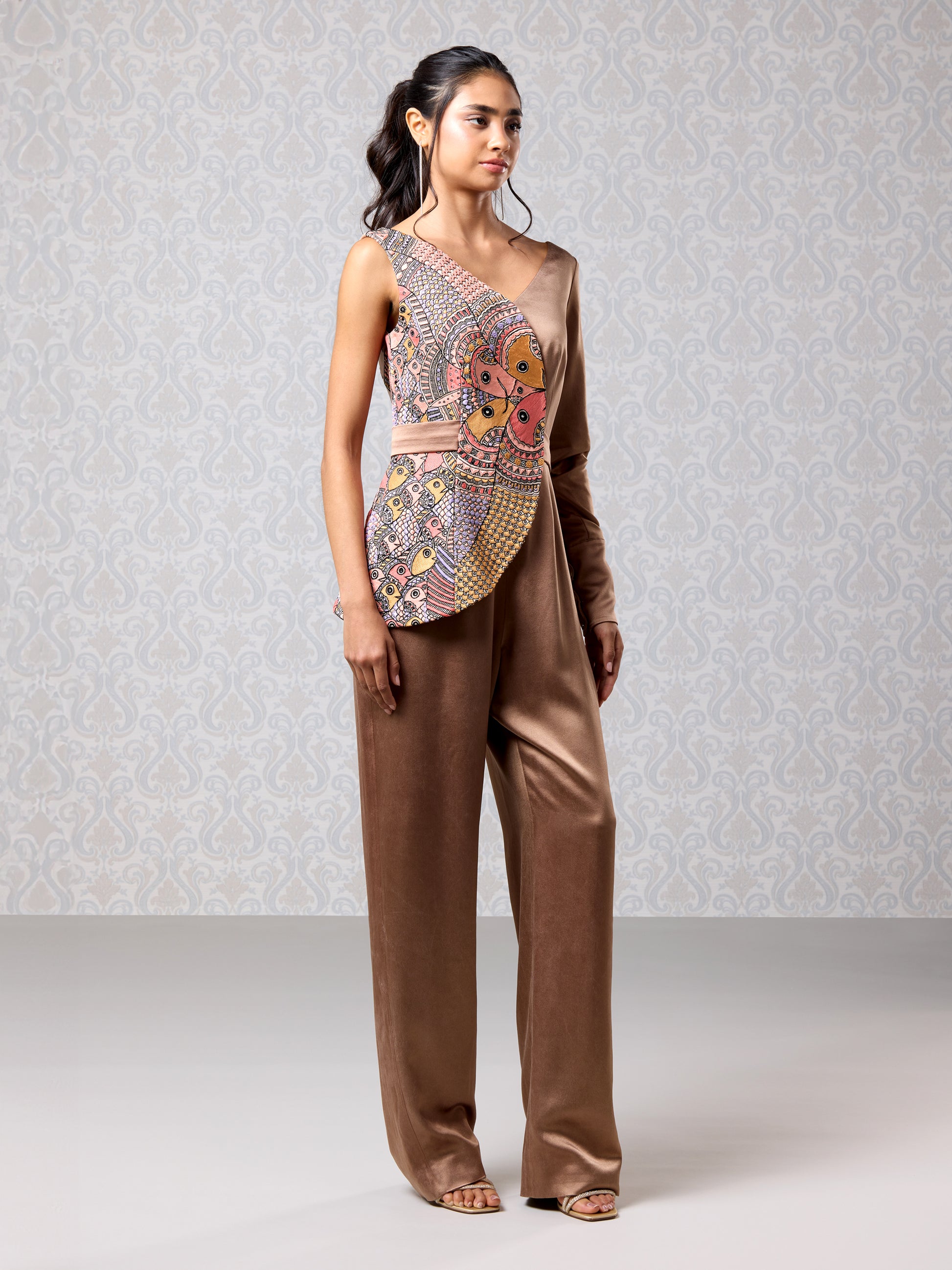 Side pose of brown oak satin jumpsuit with colorful embroidery and one-sleeve detail