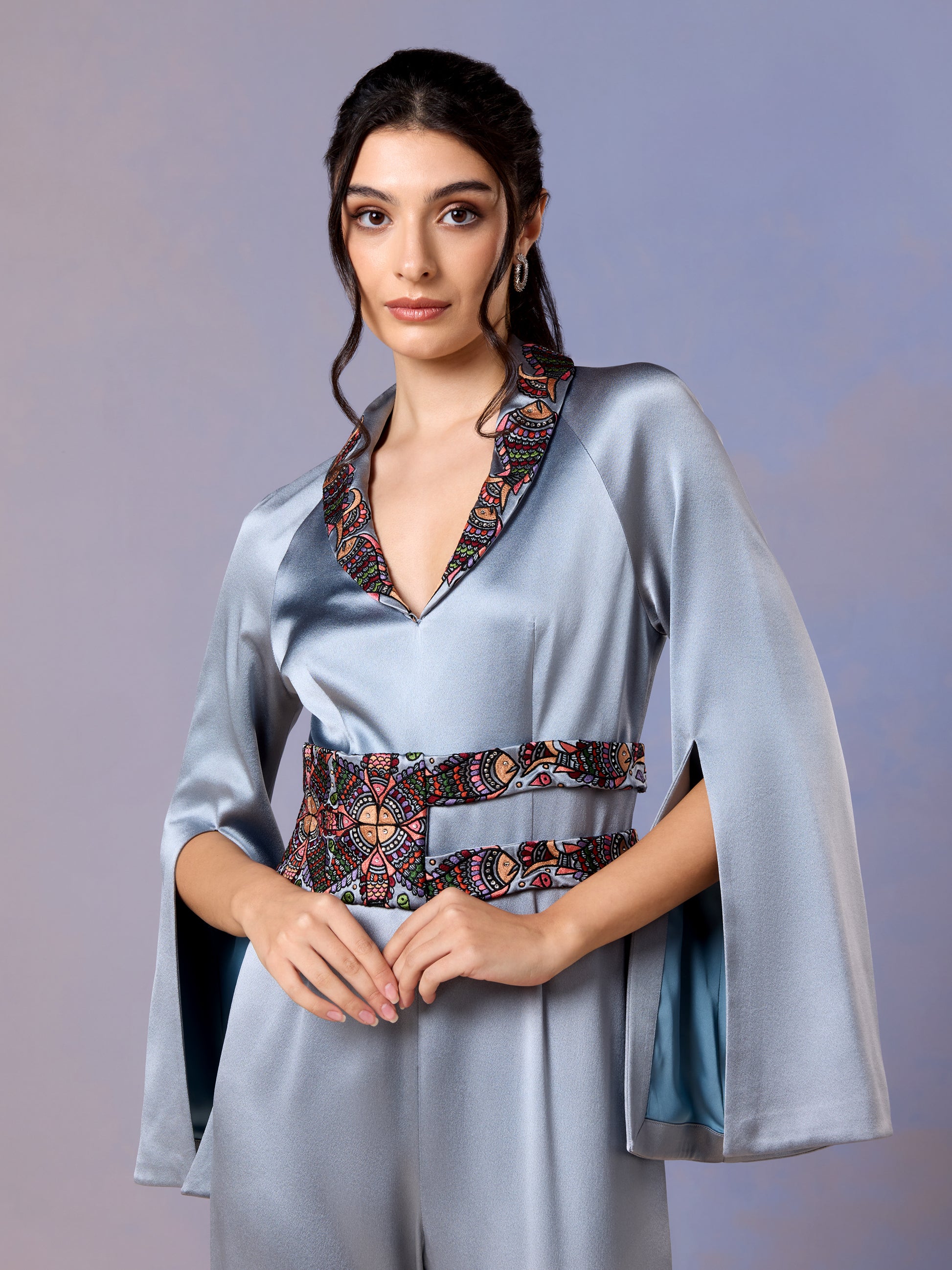 Women in glacier blue jumpsuit with cape sleeves and floral embroidered belt