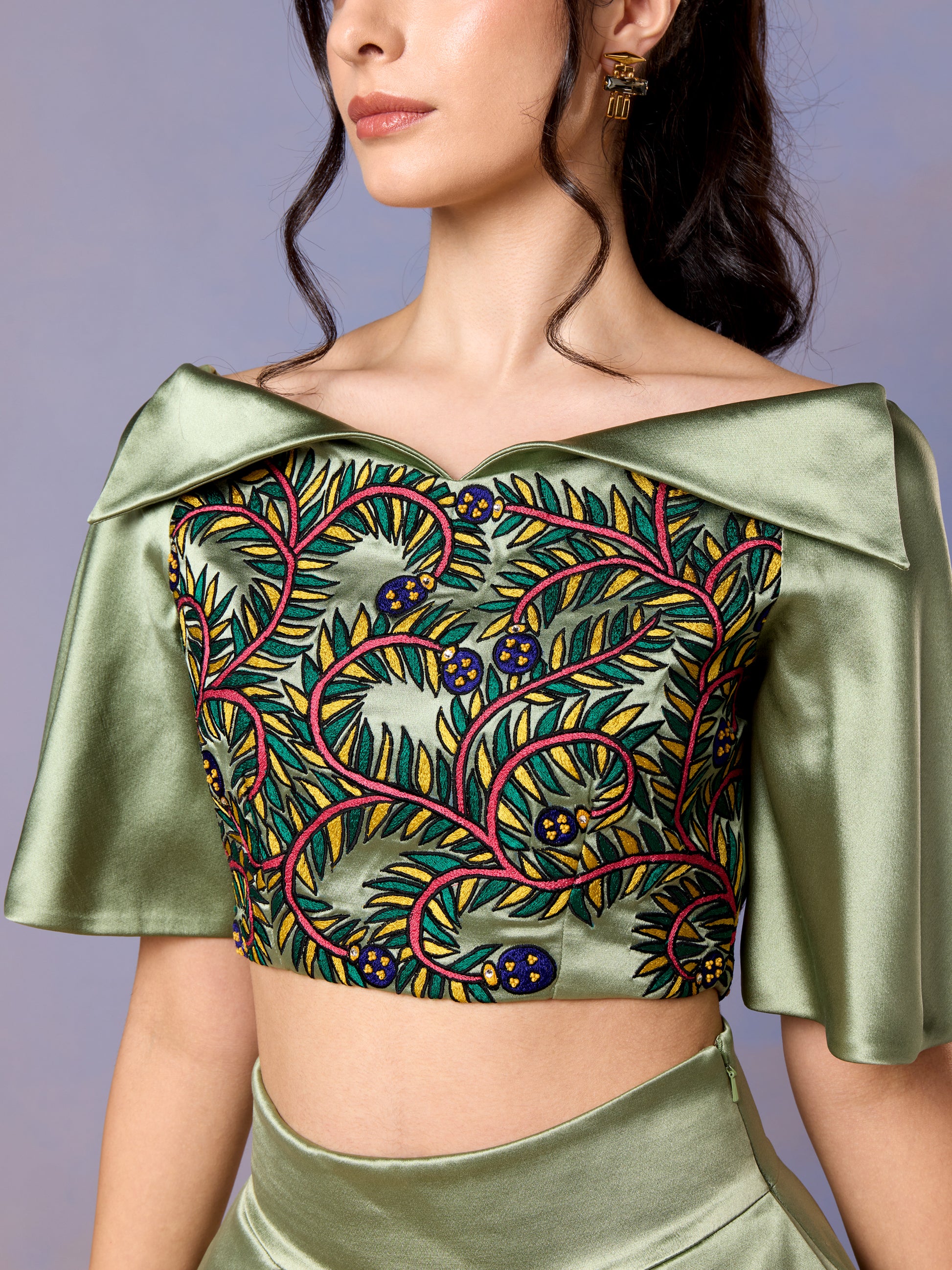 Close-up of off-shoulder sage crop top with intricate multicolor embroidery