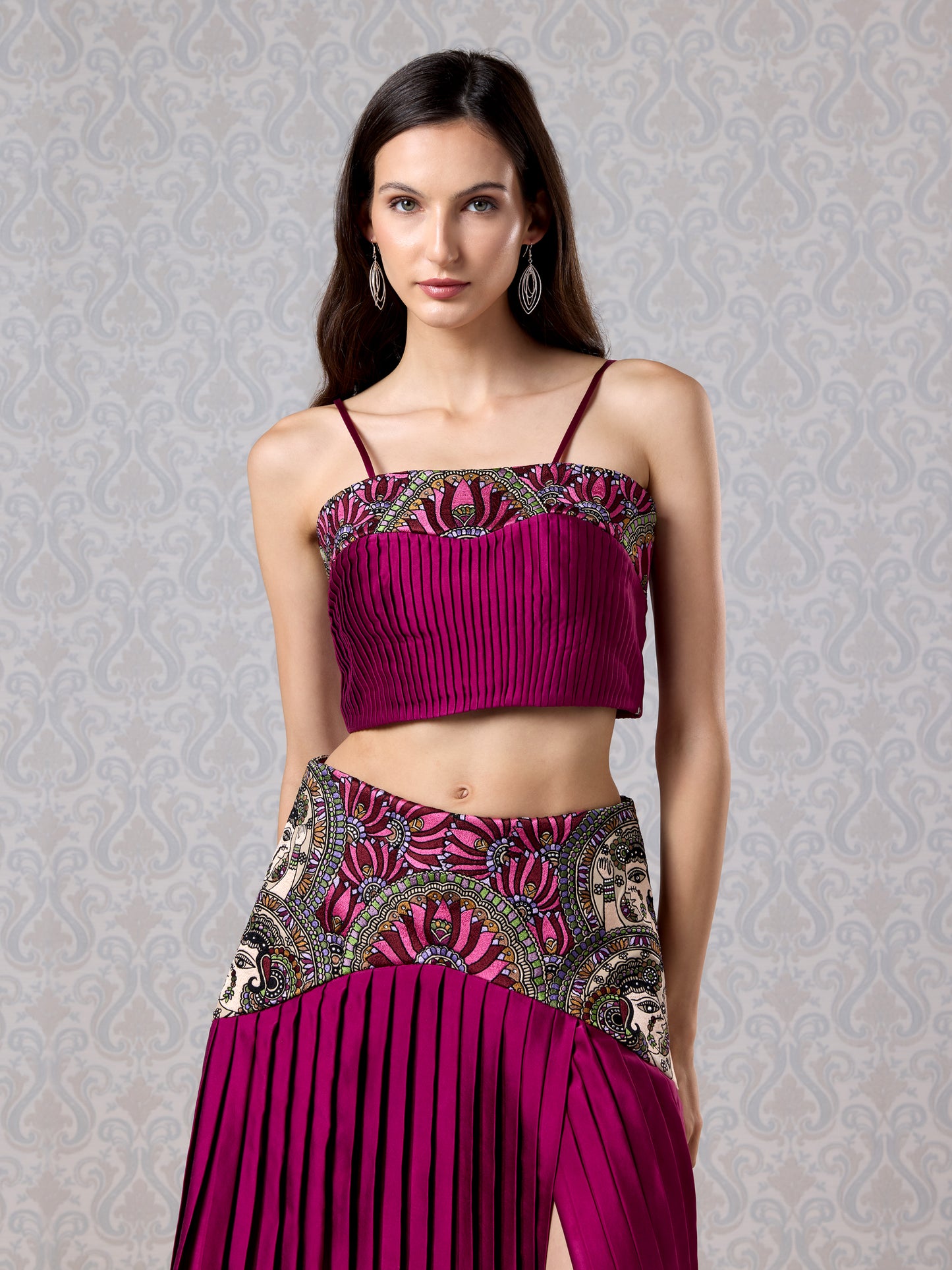 Model in cranberry satin top and asymmetric pleated skirt with leather patchwork