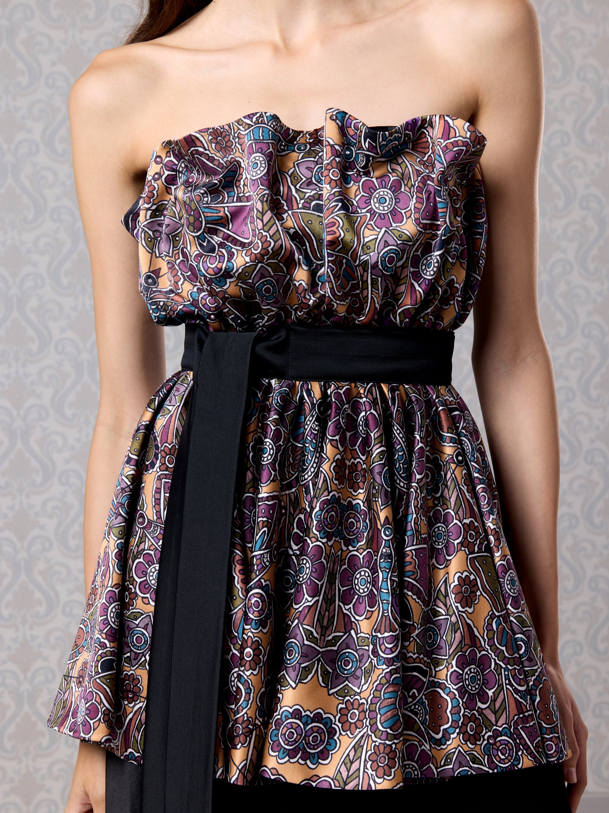 Close-up of strapless pleated printed top with black belt on silk satin gown
