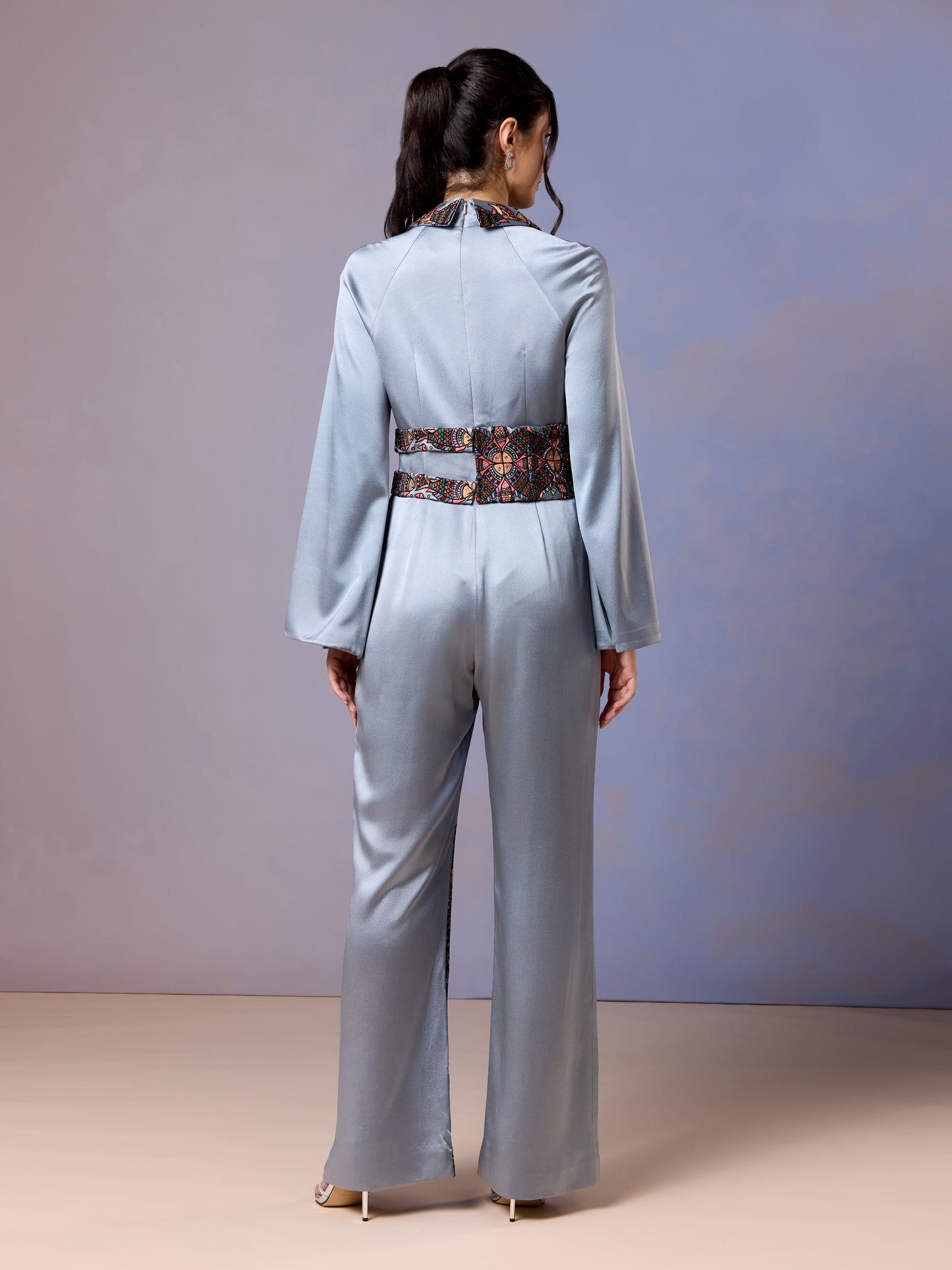 Back view of glacier blue satin jumpsuit with embroidered belt and cape detail