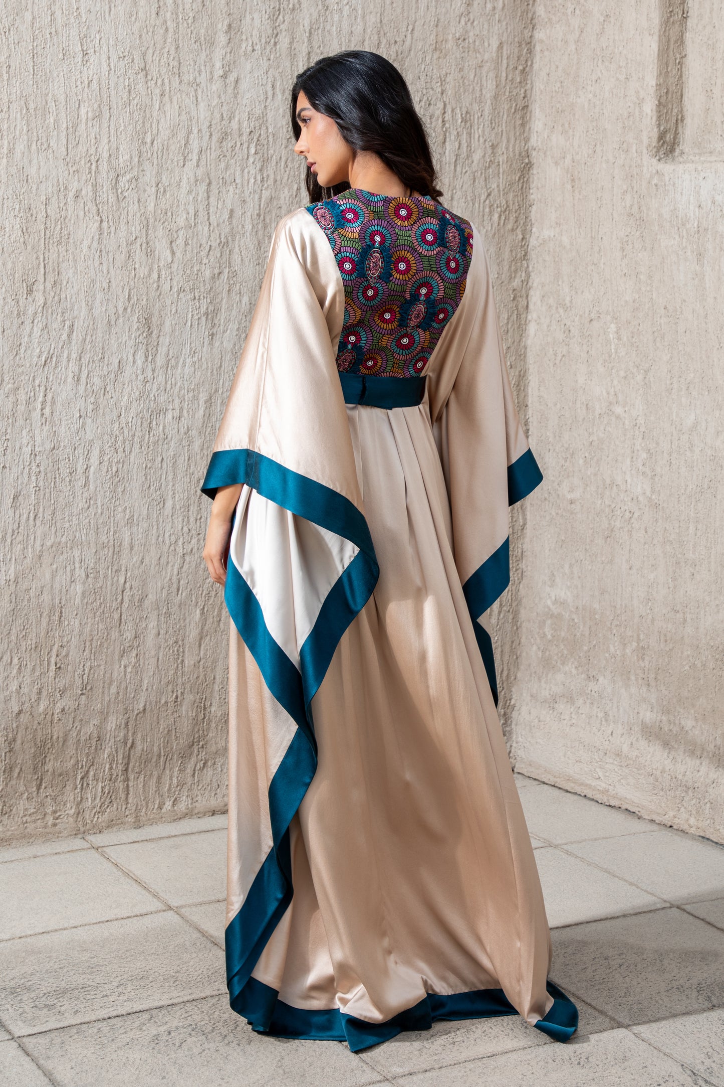 Angled view of flowy vanilla kaftan with blue accents and vibrant embroidery