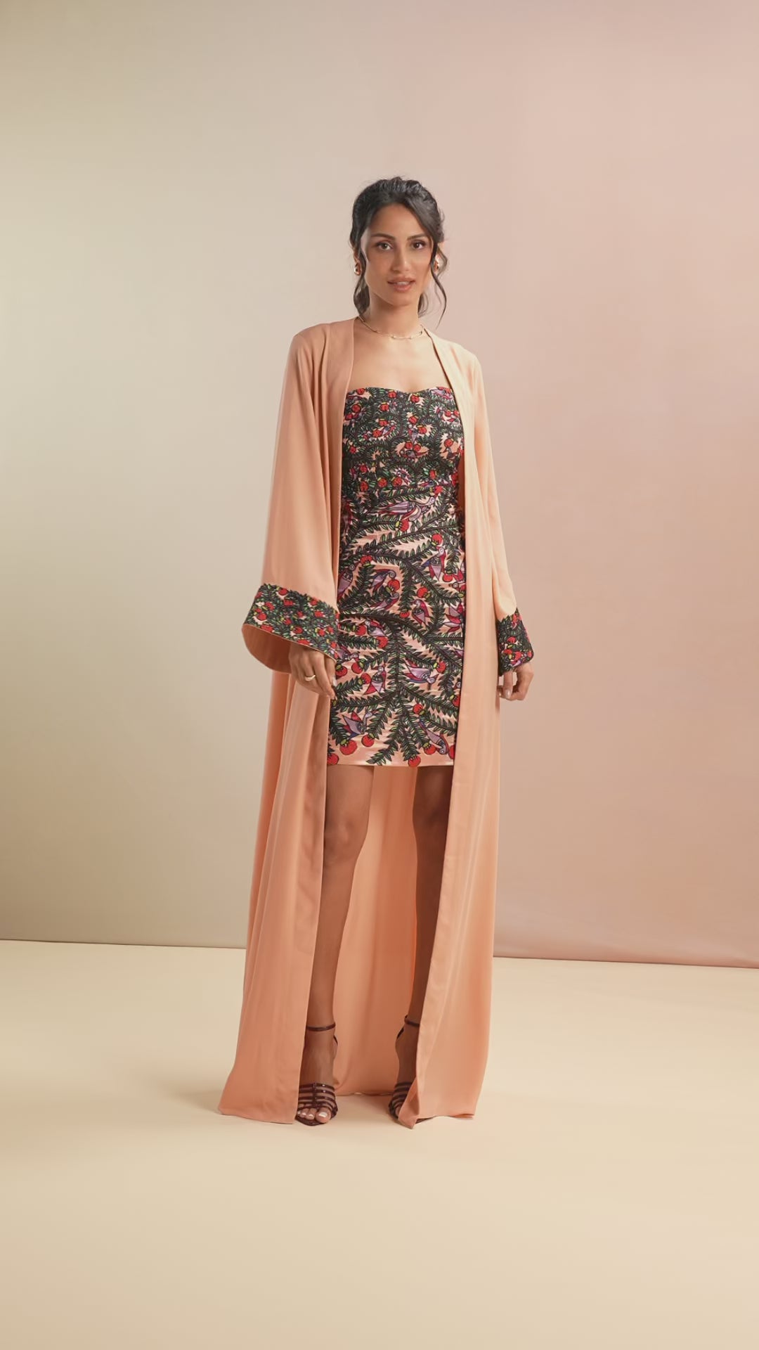 Model styling floral mini dress with peach long cape on runway