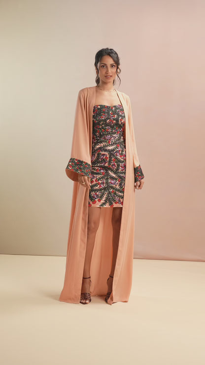 Model styling floral mini dress with peach long cape on runway