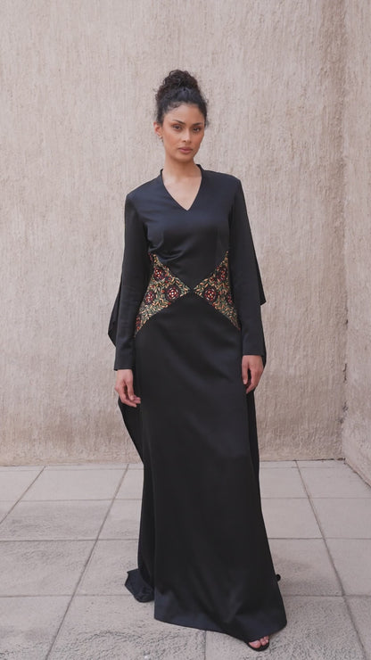 Model walking in black cape evening gown with colorful embroidery details